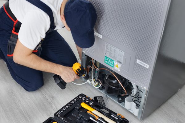 Male technician repairs a refrigerator in the kitchen in close-up. Male technician repairs a refrigerator in the kitchen in close-up.